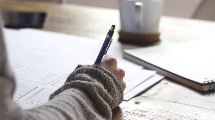 A person writing on a piece of paper with a coffee cup in front of them