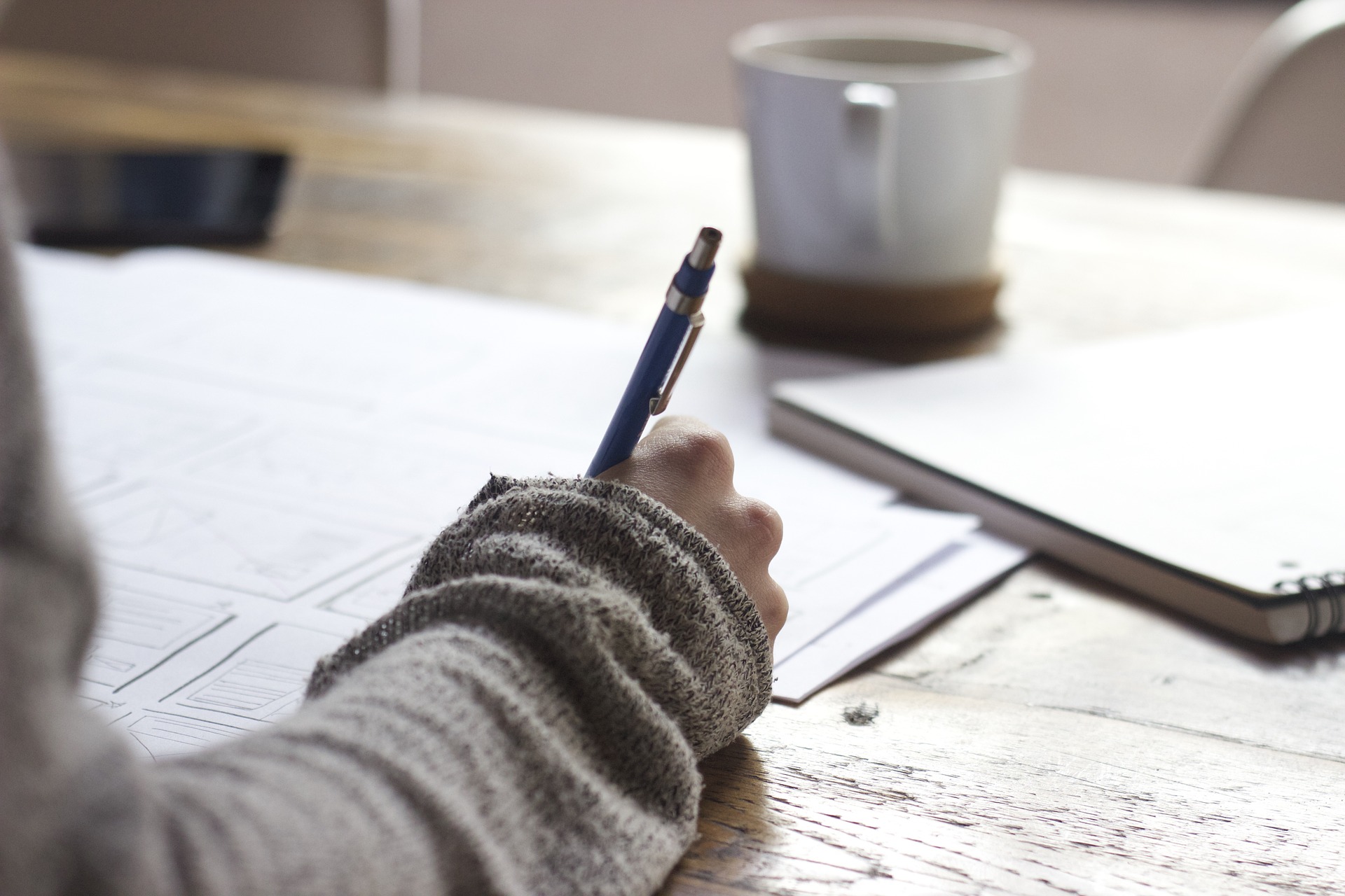 A person writing on a piece of paper with a coffee cup in front of them